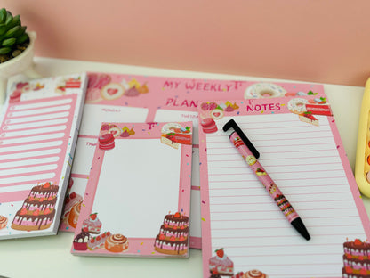 Stationary Set with A5 Lined Note Pad Pink Patisserie Themed 50 Pages 120gsm, to-do list, memo pad, weekly agenda and pen, all flat on white table with cakes, donuts, eclairs and sweets designed on pages